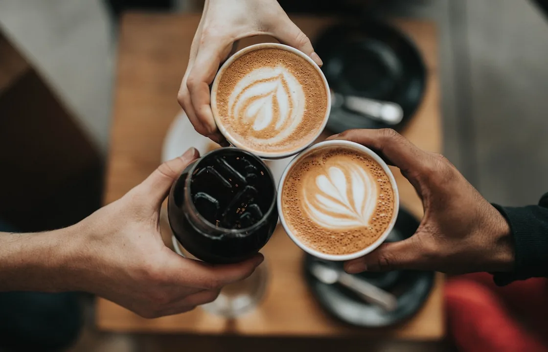 Three people bringing cups of hot and iced coffee together